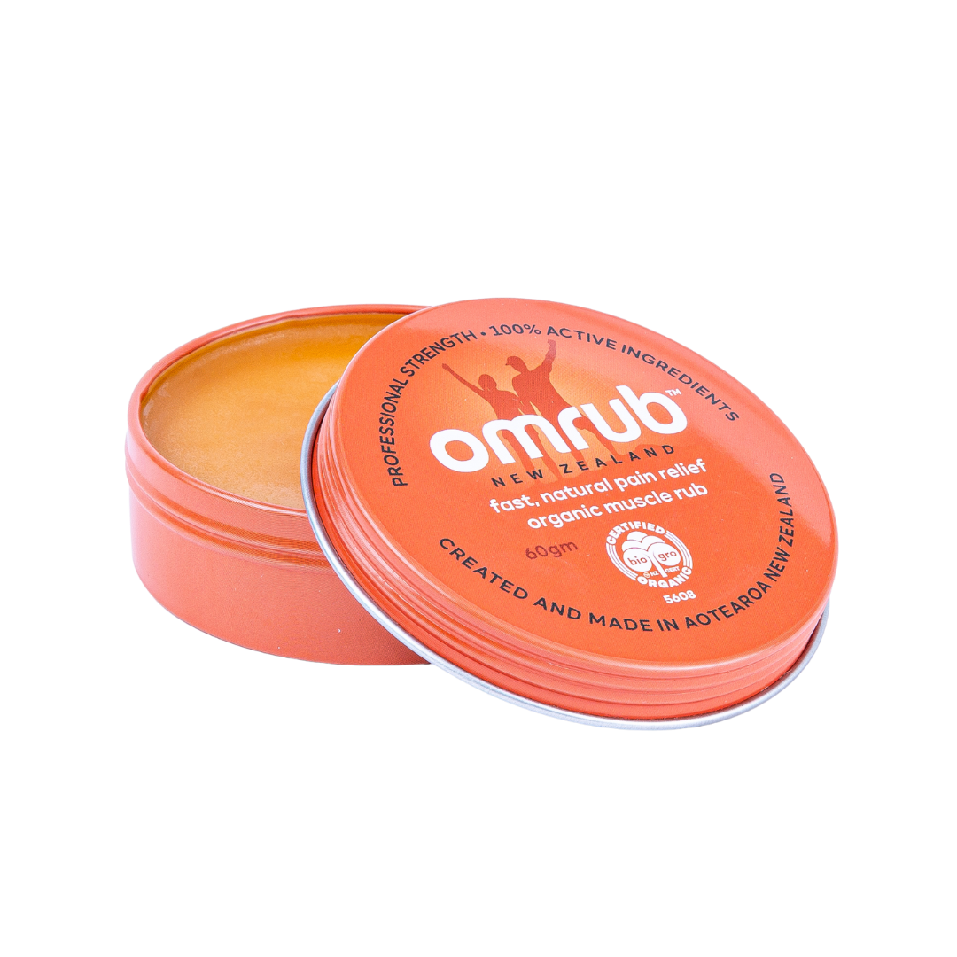 A 60g tin of Omrub organic muscle rub with the lid off, showing the balm inside. The packaging is orange with white and black text, and the product is marketed as a natural anti-inflammatory.